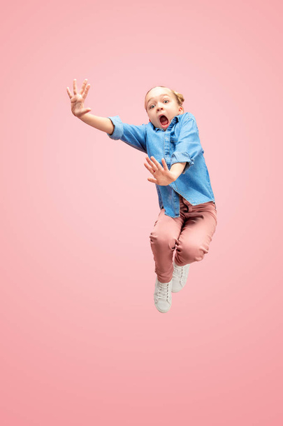 Young scared caucasian teen girl jumping in the air, isolated on pink studio background. - Фото, зображення