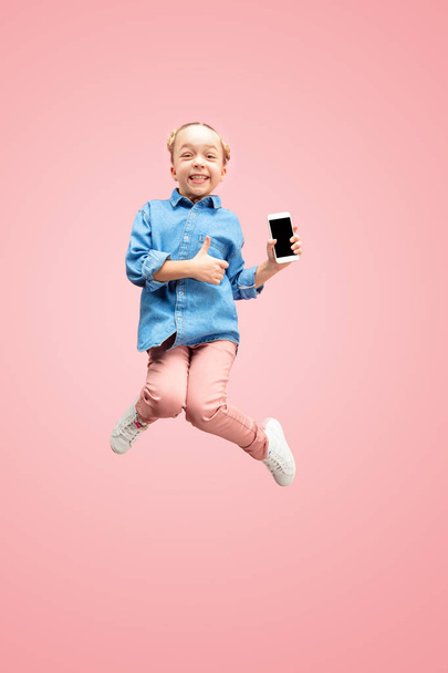 Young happy caucasian teen girl jumping with phone in the air, isolated on pink studio background. - Fotoğraf, Görsel