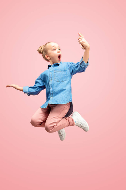 Young happy caucasian teen girl jumping with phone in the air, isolated on pink studio background. - Foto, immagini
