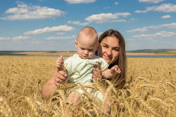 Mother with child in wheat, Young happy family in wheat field smiling and enjoying the sun - Фото, изображение