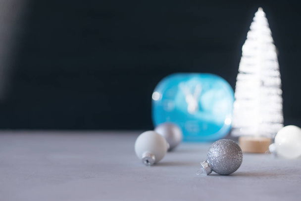 Moderne minimale Kerstmis feestelijke cadeau winter achtergrond. Close-up blauwe klok, witte kerstboom, zilveren sieraad bal op zwarte en grijze achtergrond. Xmas wenskaart, kopie ruimte, selectieve aandacht - Foto, afbeelding