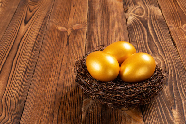 木製の背景に巣の上の金の卵 - 写真・画像