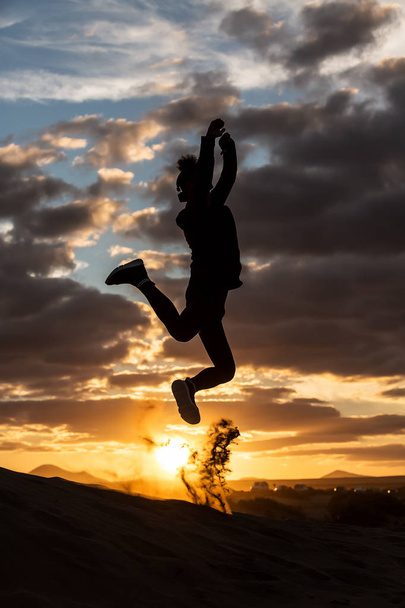 Silhouette of unrecognizable person jumping against wonderful cloudy sky in evening - Photo, Image