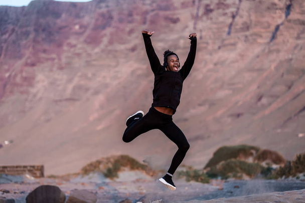 Привлекательный афроамериканец в спортивной одежде, прыгающий и кричащий от волнения, проводя время в сельской местности
 - Фото, изображение