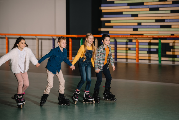 Group of smiling children skating in roller rink with holding hands - Фото, изображение