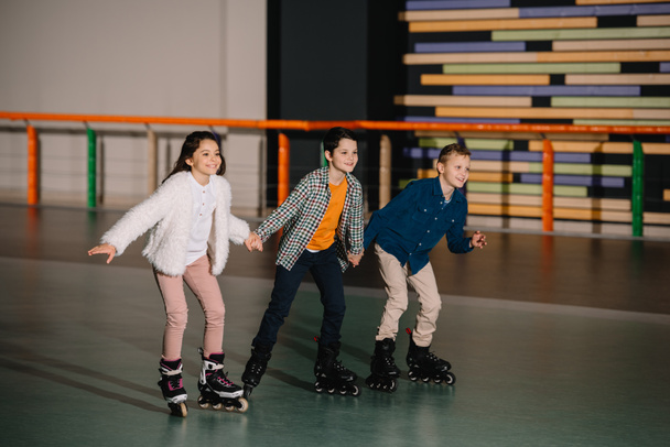 Three happy smiling children skating in roller rink with holding hands - Fotografie, Obrázek