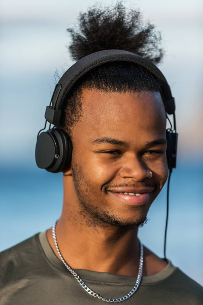 junger afrikanisch-amerikanischer Mann mit modernen Kopfhörern lächelt und schaut weg, während er Musik hört - Foto, Bild