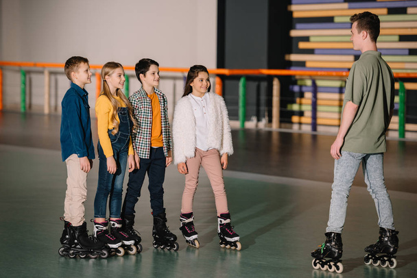 Crianças muito sorridentes em patins ouvindo atentamente as instruções do treinador
 - Foto, Imagem