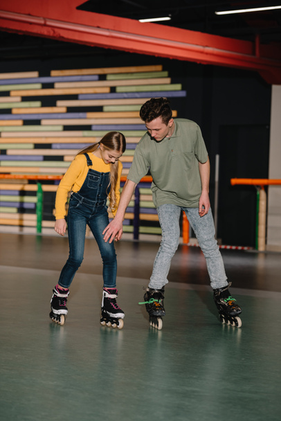 Handsome young instructor showing skating technics to attentive child - Foto, afbeelding