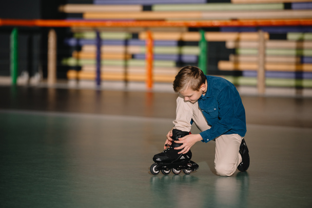 Избирательный вид симпатичного мальчика, сидящего на полу и закрепляющего ботинки на коньках
 - Фото, изображение