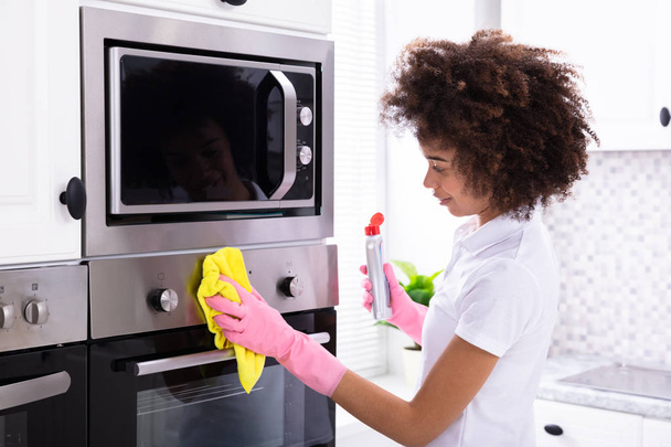 Close-up Of A Smiling Female Janitor Cleaning Oven With Yellow Napkin In The Kitchen - Photo, image