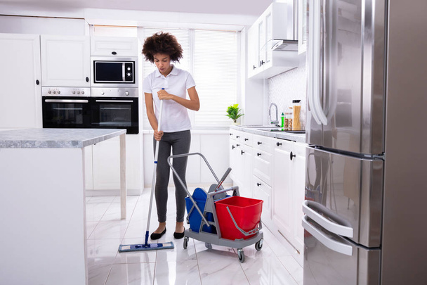 Female Janitor Cleaning The White Floor With Mop In Modern Kitchen - Foto, imagen