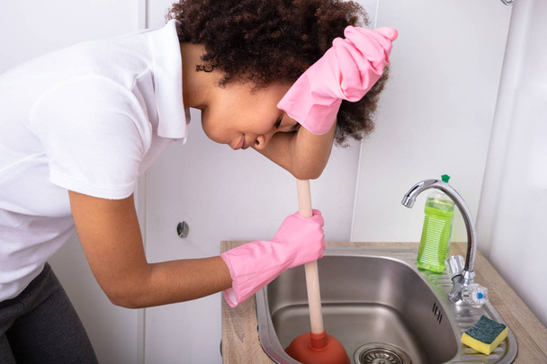 Tired Person Wearing Pink Gloves Cleaning Sink Filled With Water With Cup Plunger - Foto, Imagem