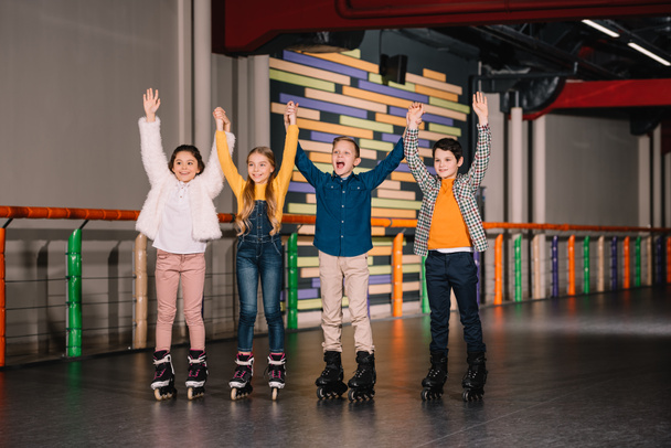 Cheerful kids in roller skates raising hands on skating rink - Fotoğraf, Görsel