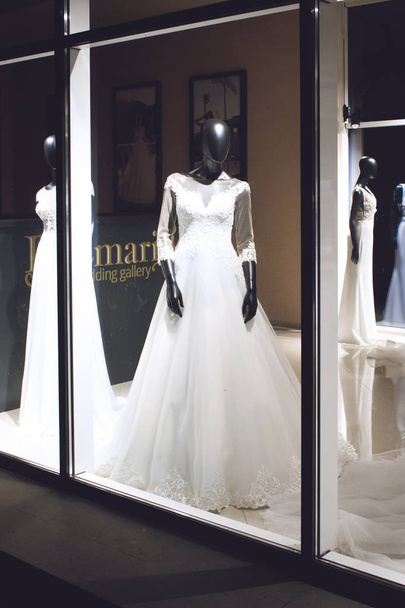  Black female mannequin in wedding dress in showcase. Bridal dresses Salon Showcase window display with light in night - Photo, Image