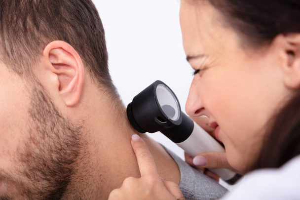 Primo piano di un giovane medico donna che controlla la pelle sul collo dell'uomo con dermatoscopio
 - Foto, immagini