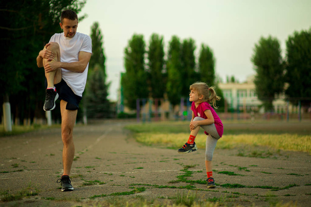 El joven padre atlético y su hija pequeña hacen ejercicios en el estadio. Estilo de vida saludable
 - Foto, Imagen