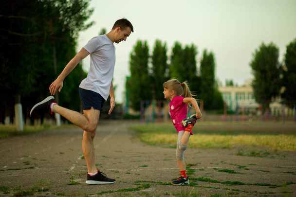 El joven padre atlético y su hija pequeña hacen ejercicios en el estadio. Estilo de vida saludable
 - Foto, Imagen