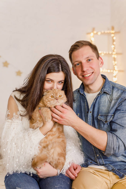 Young beautiful couple is sitting on the bed with the cat in the bright room - Valokuva, kuva