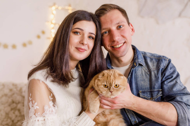 Young beautiful couple is sitting on the bed with the cat in the bright room - Fotografie, Obrázek