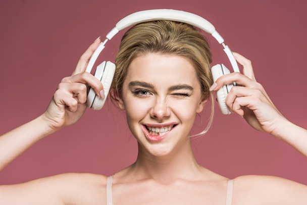 beautiful smiling girl winking and listening music with headphones, isolated on pink - Фото, зображення