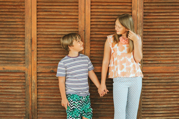 Outdoor summer portrait of two funny kids, small brother and big sister, holding hands - Photo, Image