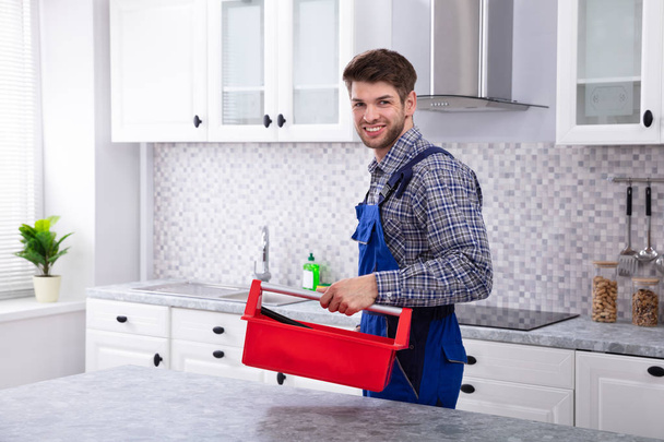 Happy Male Repairman With Red Toolbox Standing In Kitchen - Foto, imagen