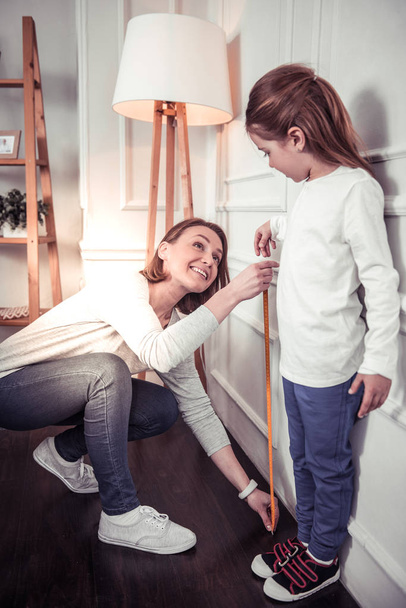 Pleasant nice woman measuring her daughters height - Photo, image