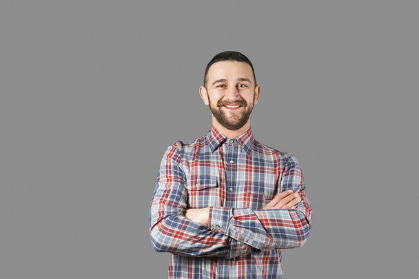 Body language concept. Young handsome man with facial hair posing over gray wall showing emotions. Portrait of masculine bearded male, wearing slim fit checkered shirt. Isolated background, copy space - Photo, Image