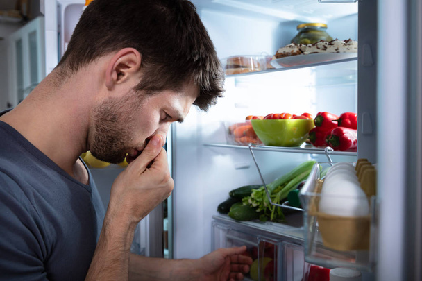 Вид збоку молодої людини розпізнає поганий запах з холодильника
 - Фото, зображення