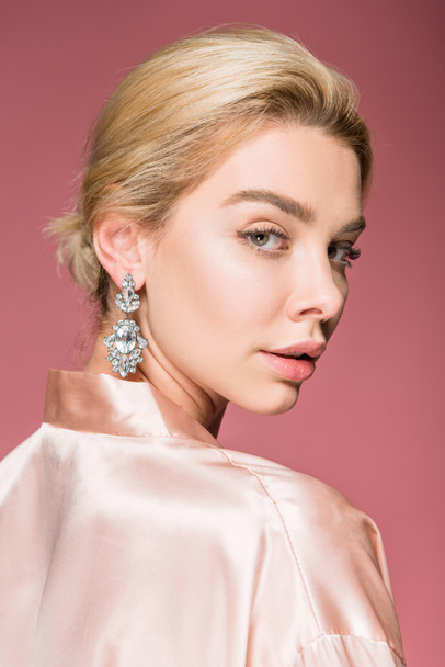 attractive blonde woman posing in earrings and silk robe, isolated on pink - Foto, afbeelding