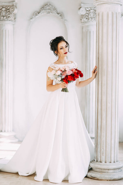 Beautiful girl in a wedding dress with a bouquet. Bride in a bright Sunny Studio. - Zdjęcie, obraz
