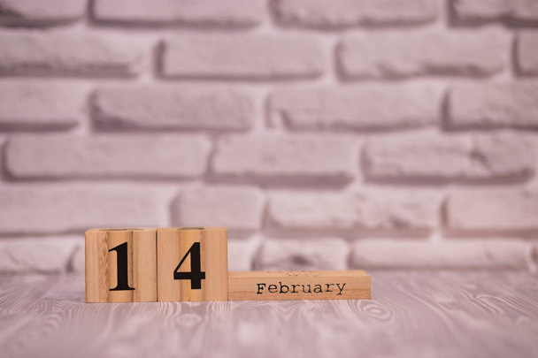 14 Φεβρουαρίου στις ξύλινες ημερολόγιο με φόντο λευκό τούβλο. - Φωτογραφία, εικόνα