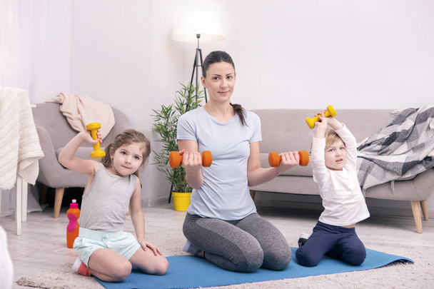 Delighted nice family lifting small dumbbells together - Фото, зображення