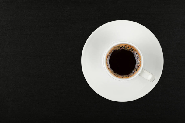 Close up one white cup full of instant coffee on saucer over black chalkboard background, elevated top view, directly above - Foto, Imagen