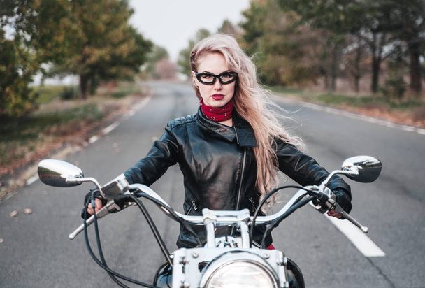 Hermosa mujer motorista posando al aire libre con la motocicleta en el camino
. - Foto, imagen