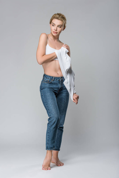 kaunis hoikka tyttö valkoinen rintaliivit riisuutuminen eristetty harmaa
 - Valokuva, kuva