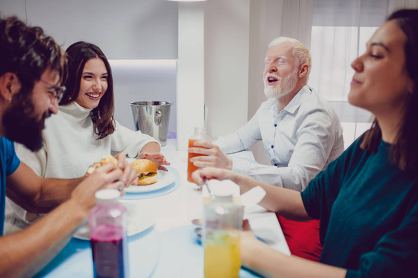 Mann bringt seine Freunde beim Mittagessen im Haus zum Lachen - Foto, Bild