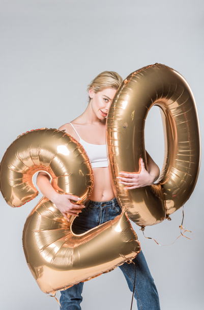 beautiful happy girl in jeans and white bra posing with 20 golden balloons, isolated on grey - Fotografie, Obrázek