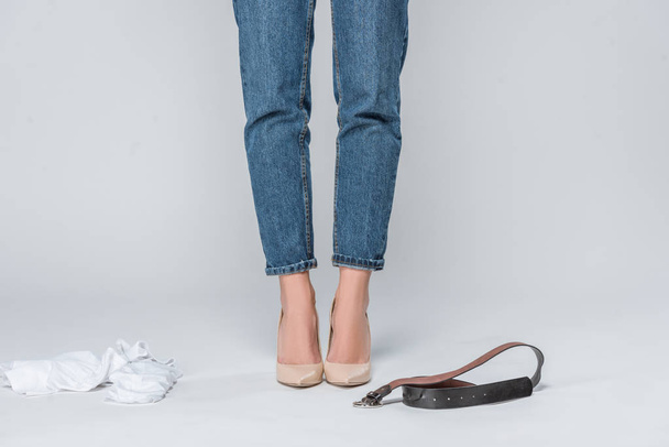low section view of woman in jeans and high heels undressing isolated on grey  - Foto, Imagen