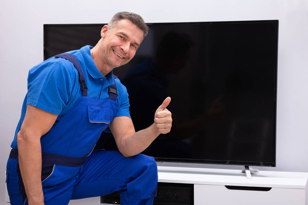 Smiling  Mature Technician Showing Thumb Up In Front Of Television - Fotó, kép