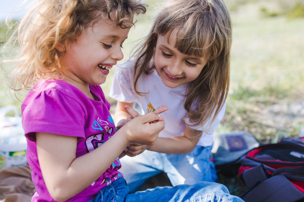 Kaksi siskoa leikkii ulkona perhosen kanssa
 - Valokuva, kuva