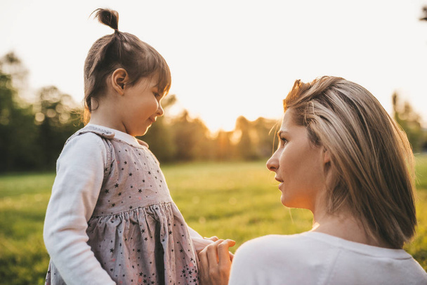 Close up view of beautiful woman have conversation with her child in the park. Rear view of mother listening her cute girl kid. Happy family. Happy Mother's Day. Motherhood and childhood - Foto, Imagem