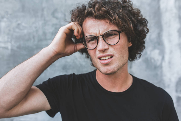 upset Uncertain handsome young man in glasses, isolated on gray concrete wall with copy space - Foto, afbeelding