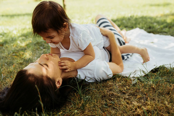 Cropped image of beautiful woman wearing striped skirt help her daughter to stand up in the park. Cute mother and her little kid playing together outdoors. Happy family. Happy Mother's Day. Motherhood - 写真・画像