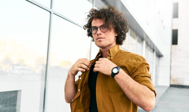 Stylish young man stundent wears shirt and wirstwatch walking on the street. Handsome male posing for advertisement with copy space outdoor in the city. People and business concept - Foto, Bild