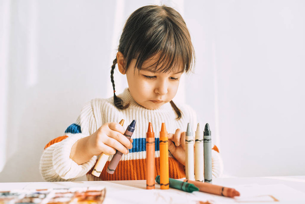 Porträt eines kreativen süßen kleinen Mädchens, das mit Ölstiften spielt und zeichnet - Foto, Bild