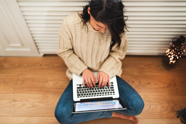 Overhead shot of young woman shopping online on laptop in cozy christmas interior. Pretty female wears sweater, sitting on the floor, prepare gifts for xmas, bying on winter sales. Copy space. - Photo, Image