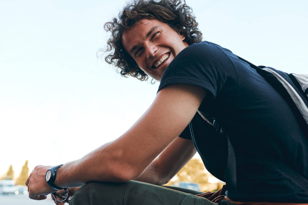 Rear view of smiling cheerful young man wears black t-shirt and wristwatch on the city street. Happy male with curly hair posing for advertisement with copy space outdoor. People concept - Photo, Image