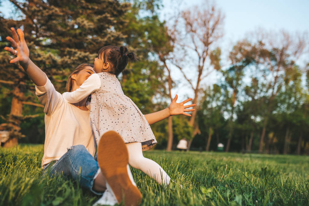 Joyful happy girl kid playing with her mother outdoor. Portrait of happy woman and her cute child embracing in the park. Happy family emotion. Happy Mother's Day. Motherhood and childhood. - 写真・画像